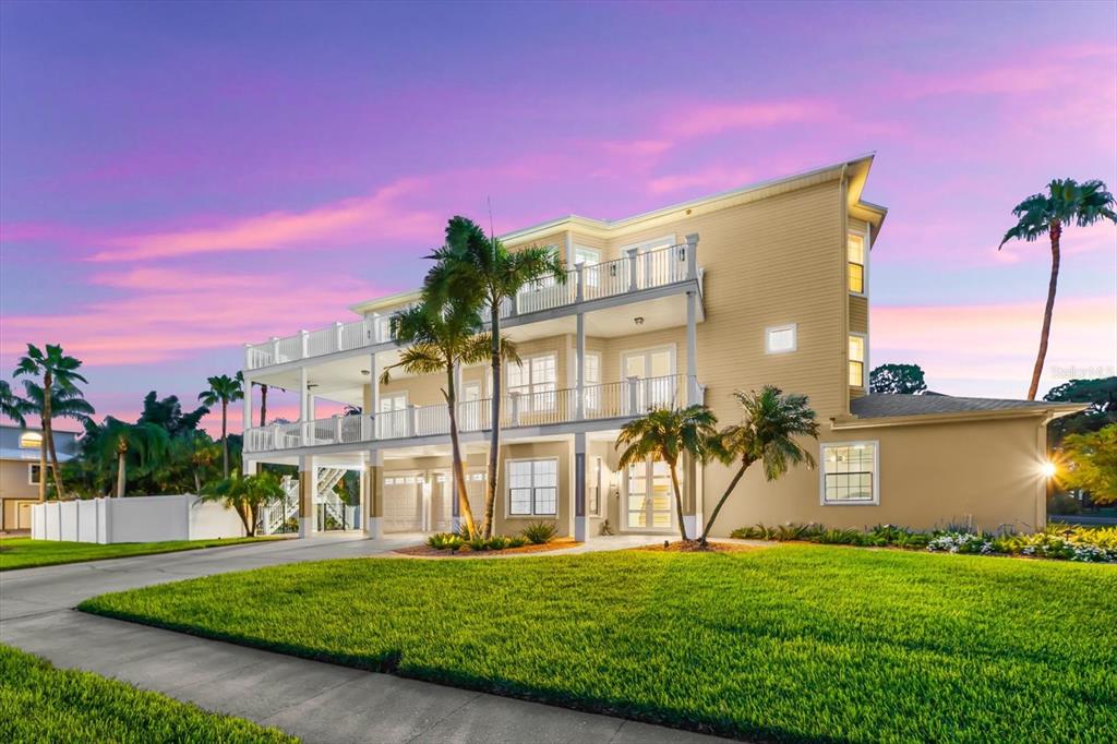 A three-story tan house with multiple balconies and a large lawn at sunset — 1700 OYSTER POINT WAY, PALM HARBOR, FL