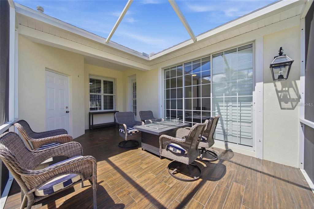 A screened-in patio features wood-look tile flooring, a fire pit table, and wicker seating — 5610 GOLDEN ISLES DRIVE, APOLLO BEACH, FL