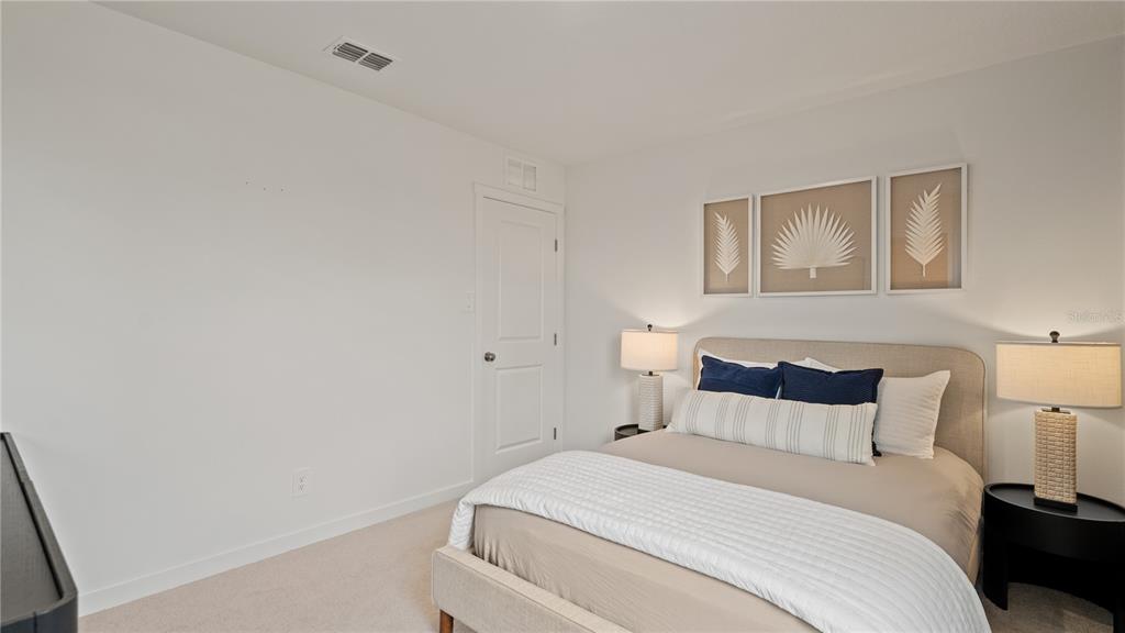 A bedroom features a bed with neutral bedding, two bedside lamps, and framed wall art — 6105 SWAMP BAY DRIVE, EDGEWATER, FL