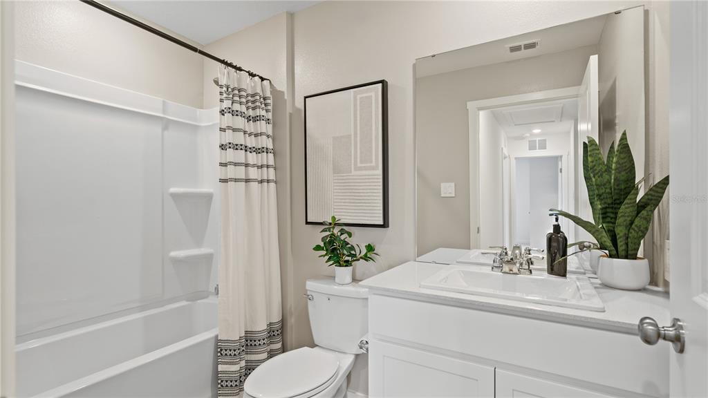 A bathroom features a white vanity, a toilet, a shower-tub combination, and a framed wall art — 6105 SWAMP BAY DRIVE, EDGEWATER, FL