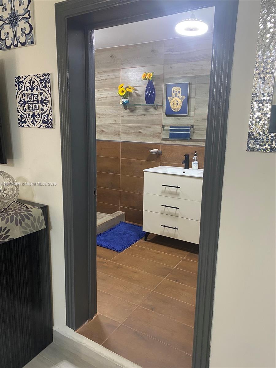 A bathroom features wood-look tile walls, a white vanity, and a blue hamsa wall art — 6 CALLE 29 ESTE, NY 10133, NY