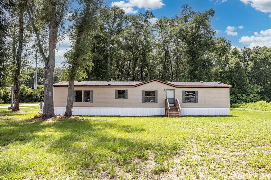 A single-story manufactured home with tan siding sits on a grassy lot near trees — 968 CR222 ROAD, OXFORD, FL