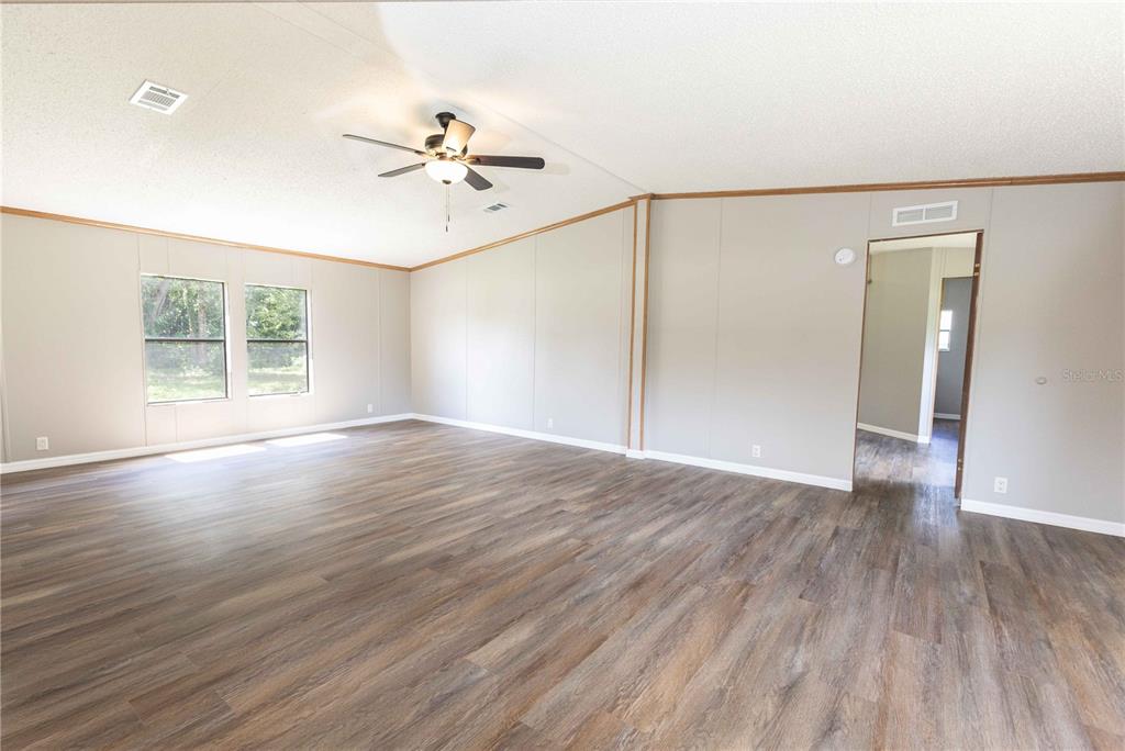 An empty living room features light-colored walls, wood-look flooring, a ceiling fan, and two windows — 968 CR222 ROAD, OXFORD, FL