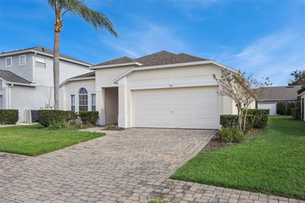 A single-story house with a beige stucco exterior, a two-car garage, and a paver driveway — 746 KILDRUMMY DRIVE, DAVENPORT, FL