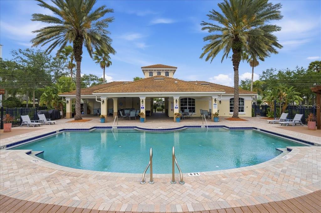 A swimming pool sits in front of a clubhouse with a tiled roof and palm trees — 7903 SEMINOLE BOULEVARD UNIT 2305, SEMINOLE, FL