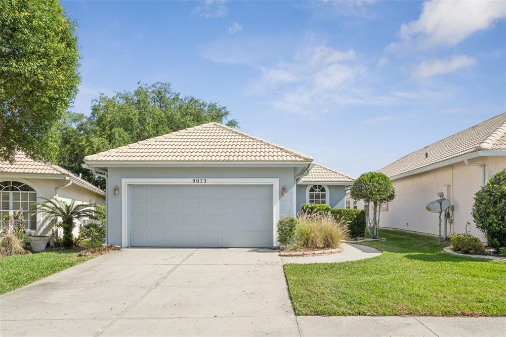 A single-story house with a light gray exterior, a two-car garage, and a tiled roof — 9073 SAINT ANDREWS WAY, MOUNT DORA, FL