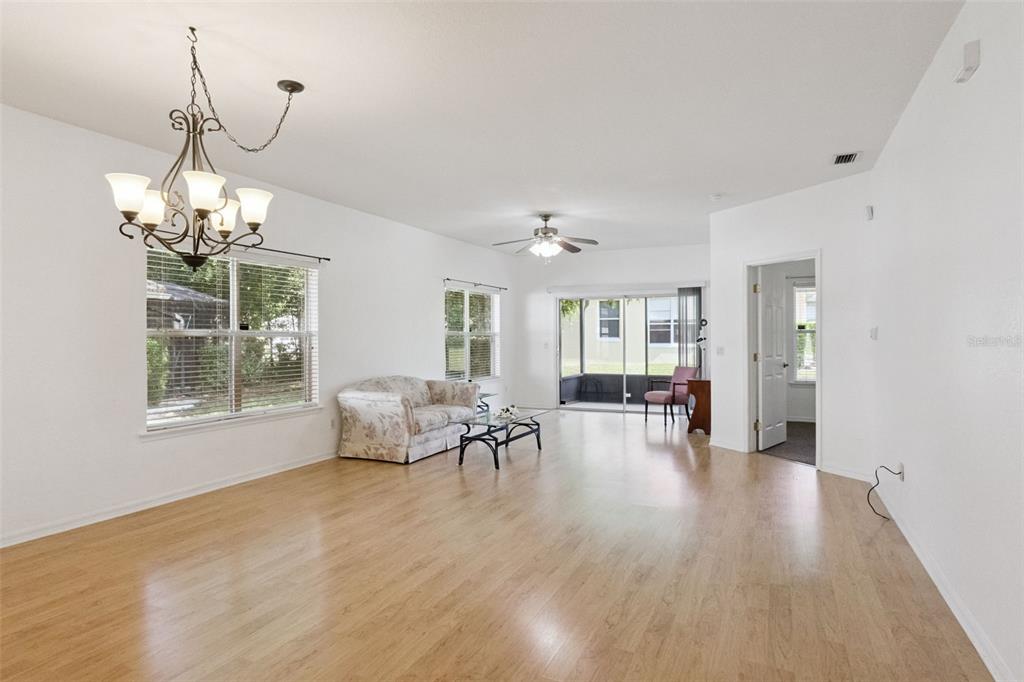 A living room with light wood flooring, a chandelier, a ceiling fan, and sliding doors — 9073 SAINT ANDREWS WAY, MOUNT DORA, FL