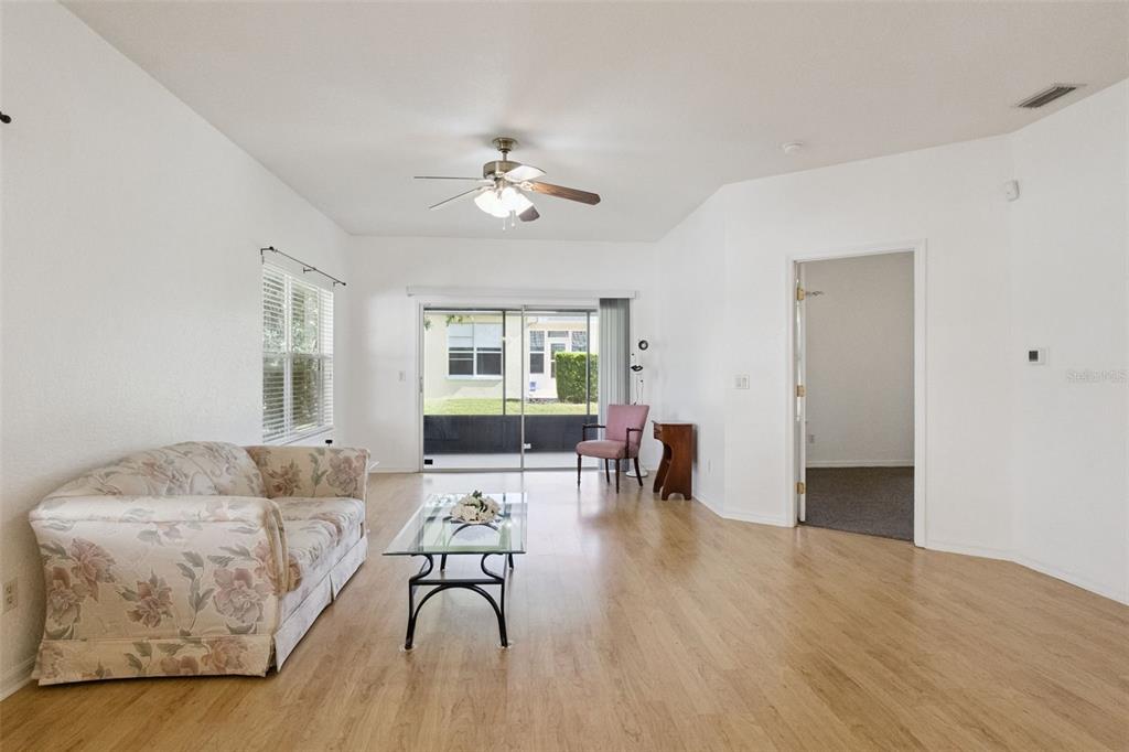 A living room with light wood flooring, a floral sofa, glass coffee table, and sliding doors — 9073 SAINT ANDREWS WAY, MOUNT DORA, FL