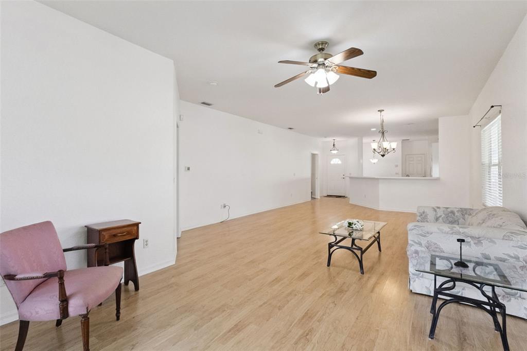 A living room features light wood flooring, white walls, a ceiling fan, and sparse furniture — 9073 SAINT ANDREWS WAY, MOUNT DORA, FL