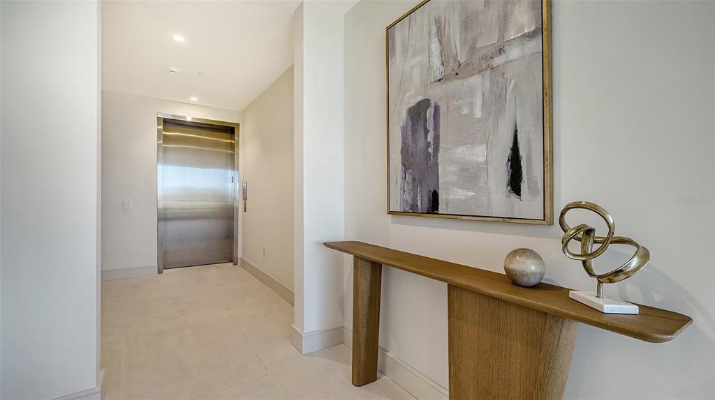 A modern hallway features a stainless steel elevator, a wooden console table, and abstract wall art — 1591 GULF OF MEXICO DRIVE UNIT 313, LONGBOAT KEY, FL