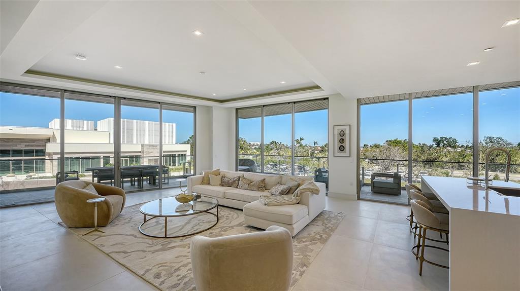 A modern living room features floor-to-ceiling windows, a white sectional sofa, and light tile flooring — 1591 GULF OF MEXICO DRIVE UNIT 313, LONGBOAT KEY, FL
