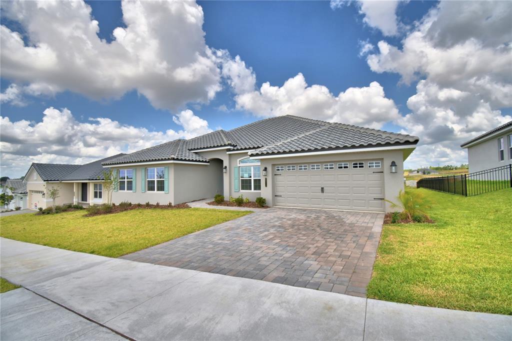 A single-story house with a gray tile roof, beige stucco walls, and a paver driveway — 4270 JULIANA LAKE DRIVE, AUBURNDALE, FL