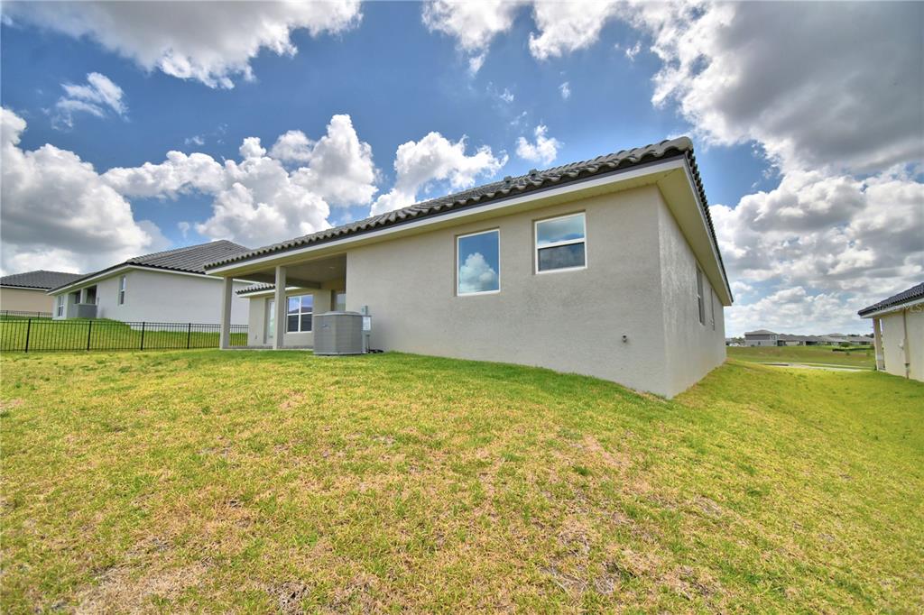 The exterior rear view of a beige house features a covered patio and grassy yard — 4270 JULIANA LAKE DRIVE, AUBURNDALE, FL