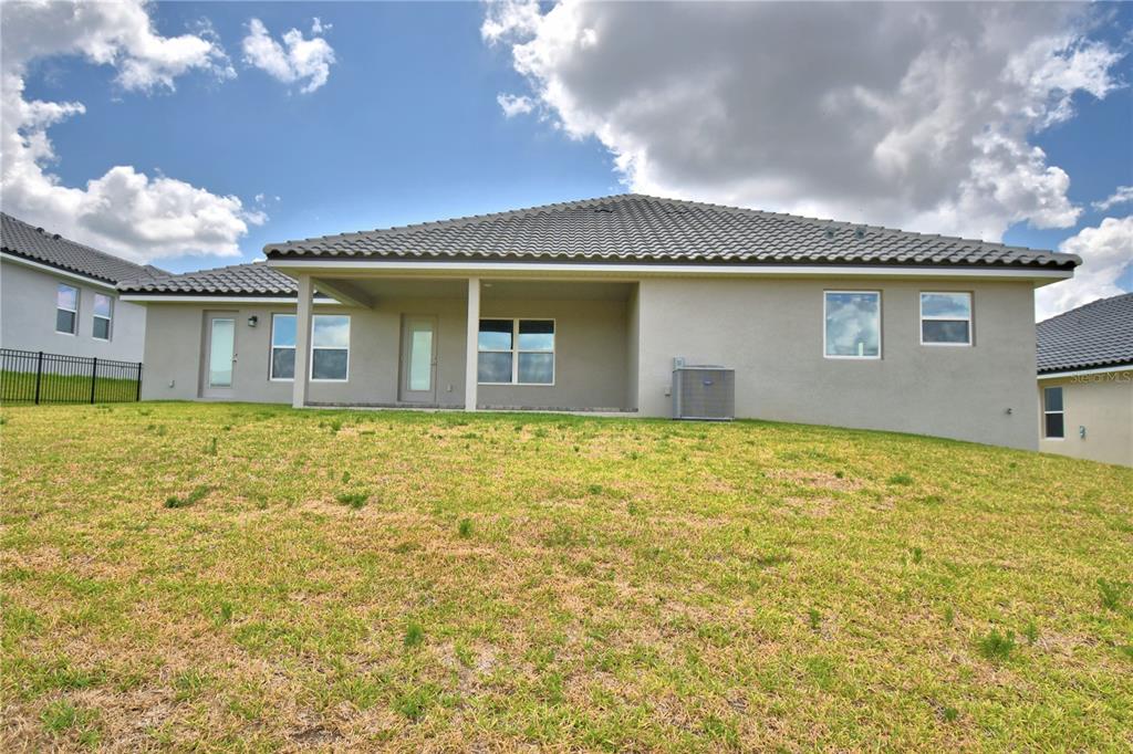 The rear exterior of a single-story house features a covered patio and a grassy yard — 4270 JULIANA LAKE DRIVE, AUBURNDALE, FL
