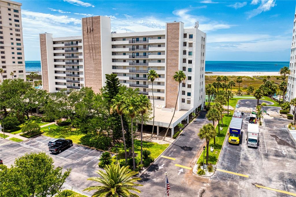 An aerial view shows a multi-story apartment building with a parking lot and beach access — 1250 GULF BOULEVARD UNIT 302, CLEARWATER BEACH, FL