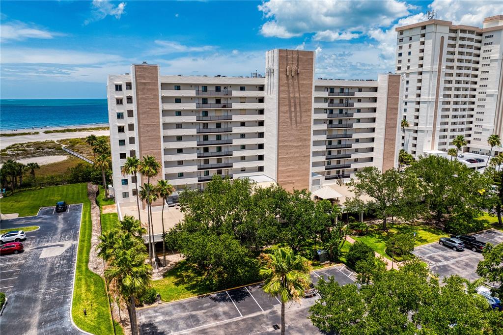 An aerial view shows a multi-story apartment building situated near a beach and ocean — 1250 GULF BOULEVARD UNIT 302, CLEARWATER BEACH, FL