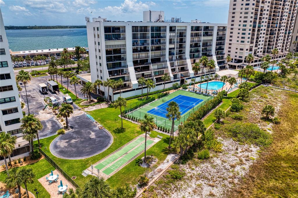 An aerial view shows a multi-story apartment building with a tennis court and swimming pool — 1250 GULF BOULEVARD UNIT 302, CLEARWATER BEACH, FL