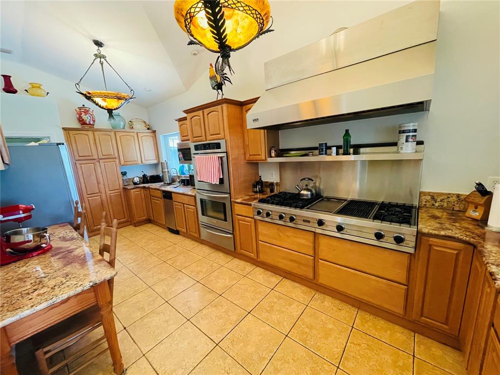 A kitchen features wood cabinetry, stainless steel appliances, a large range hood, and tile flooring — 807 NEPTUNE ROAD, KISSIMMEE, FL