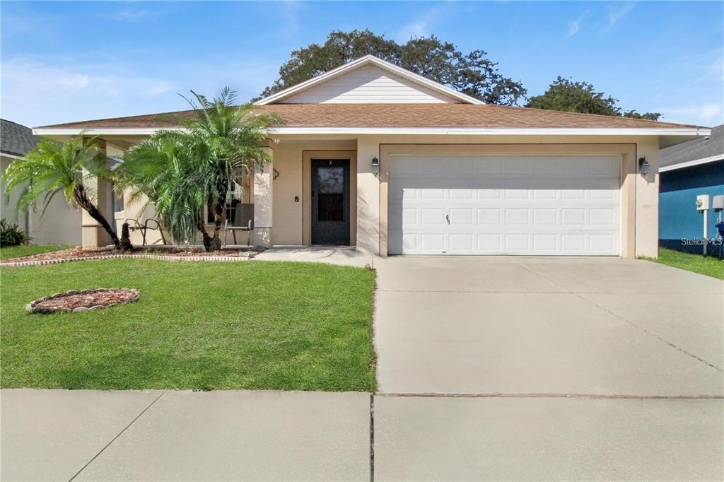 A single-story house with a beige stucco exterior, a two-car garage, and a palm tree — 15427 WINTER BREEZE LANE, WIMAUMA, FL