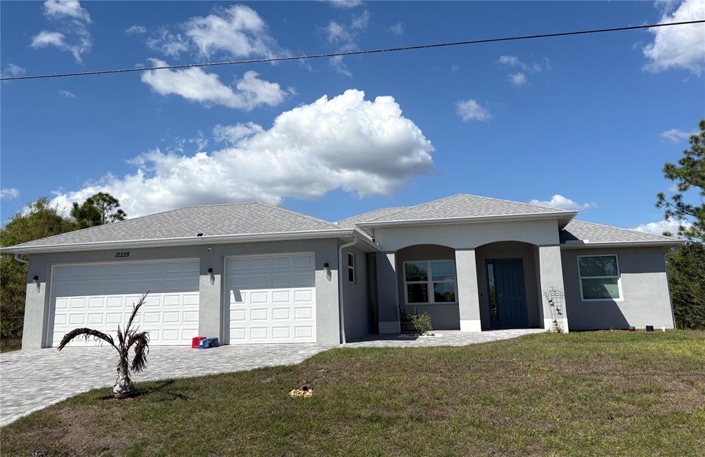 A single-story gray house with a two-car garage and a paved driveway under a blue sky — 7194 PINEDALE DRIVE, PORT CHARLOTTE, FL