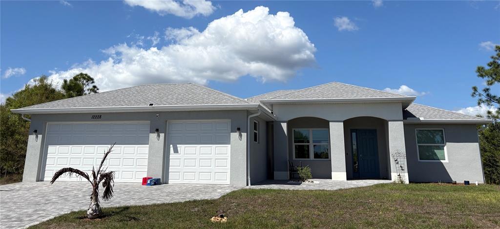 A single-story house with a gray stucco exterior, a three-car garage, and a paved driveway — 7194 PINEDALE DRIVE, PORT CHARLOTTE, FL