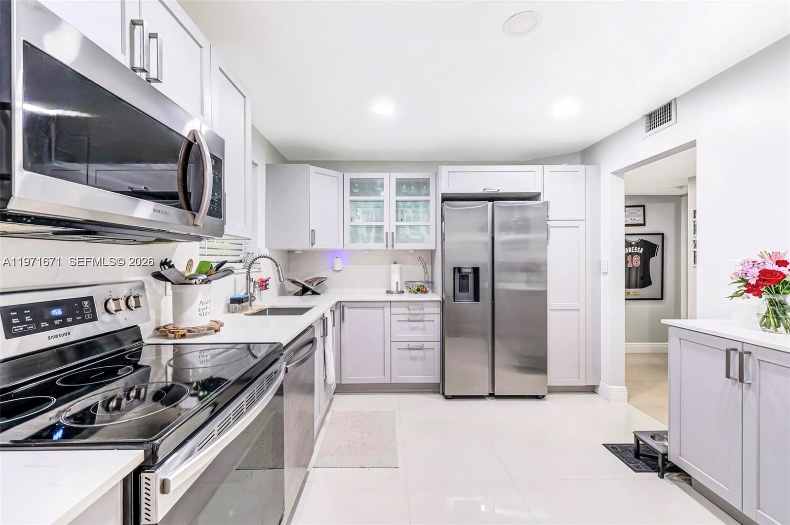 A modern kitchen features white cabinetry, stainless steel appliances, and light-colored tile flooring — 601 Ives Dairy Rd # 00, Miami FL 33179, MIAMI, FL