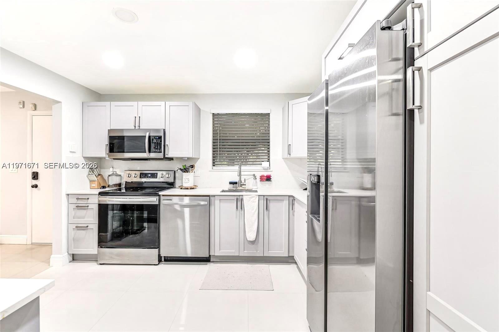 A modern kitchen features white cabinets, stainless steel appliances, and light-colored tile flooring — 601 Ives Dairy Rd # 00, Miami FL 33179, MIAMI, FL