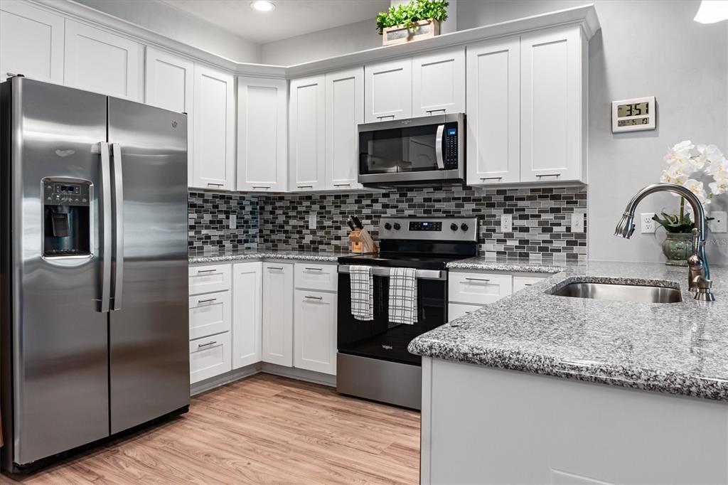 A kitchen with white cabinets, stainless steel appliances, granite countertops, and a gray tile backsplash — 1159 NW 129TH DRIVE, NEWBERRY, FL