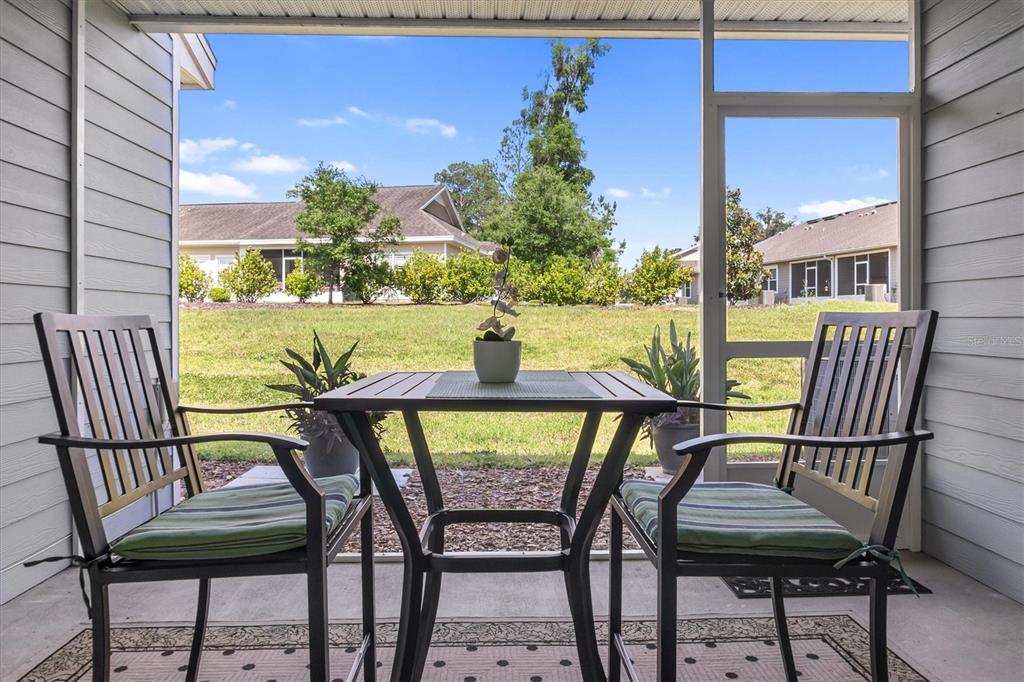 A screened-in patio features a small table and two chairs overlooking a grassy yard — 1159 NW 129TH DRIVE, NEWBERRY, FL