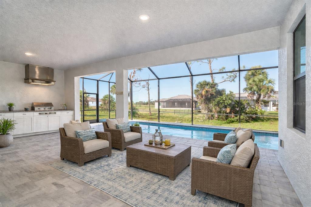 A covered outdoor patio features a kitchen, pool, and seating area on a paved deck — 237 W PINE VALLEY LANE, ROTONDA WEST, FL
