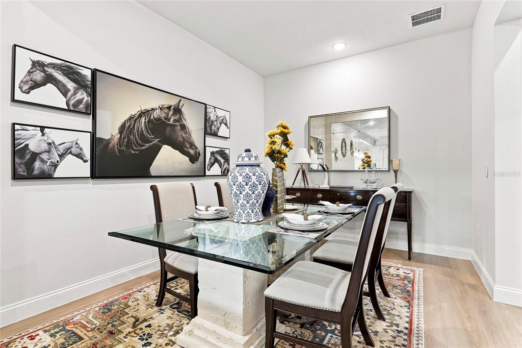 A dining room features a glass-topped table, upholstered chairs, horse-themed wall art, and a patterned rug — 3333 ARMEN DRIVE, MERRITT ISLAND, FL
