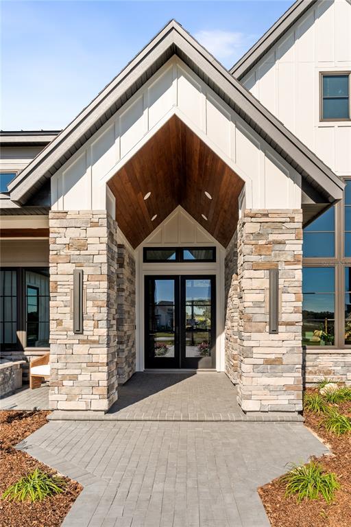 A modern home entrance features a stone-clad porch, wood-paneled ceiling, and a glass-paned double door — 12522 SW 58TH CIRCLE, ARCHER, FL