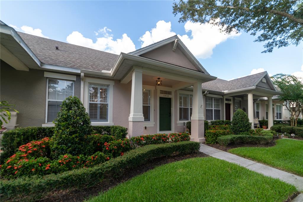 A single-story house with a covered front porch, tan stucco walls, and manicured landscaping — 13639 CEPHEUS DRIVE, ORLANDO, FL
