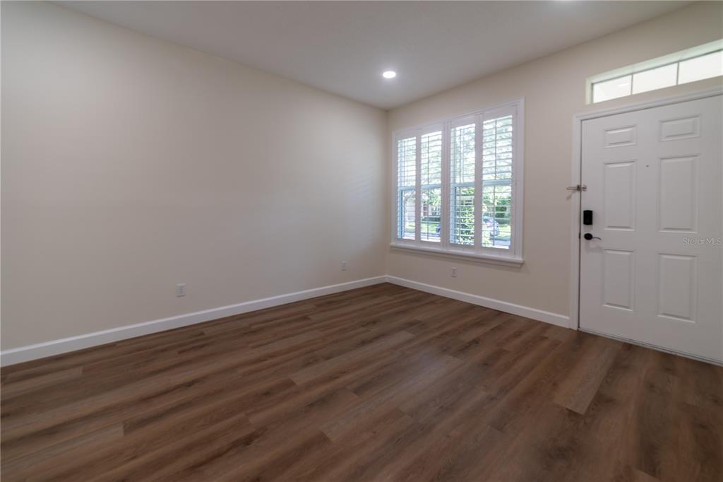 An empty room features wood-look flooring, white walls, plantation shutters, and a front entry door — 13639 CEPHEUS DRIVE, ORLANDO, FL