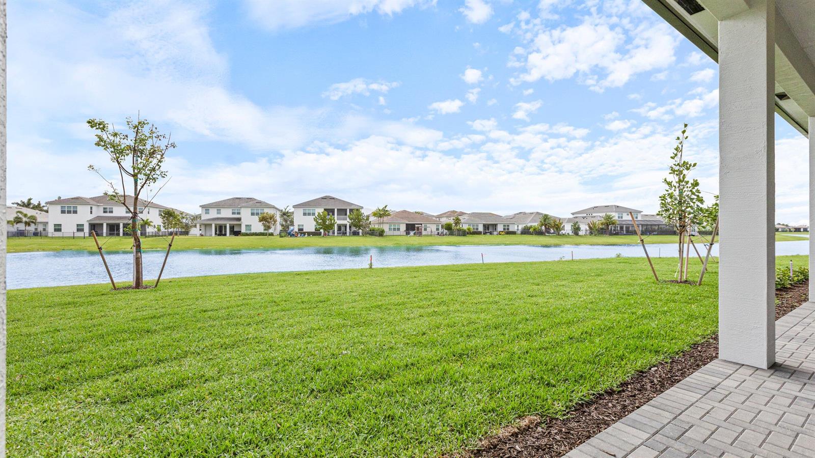 A view from a paved patio overlooking a grassy backyard and a neighborhood pond — 5474 Hutchinson Way, FL 33470, FL