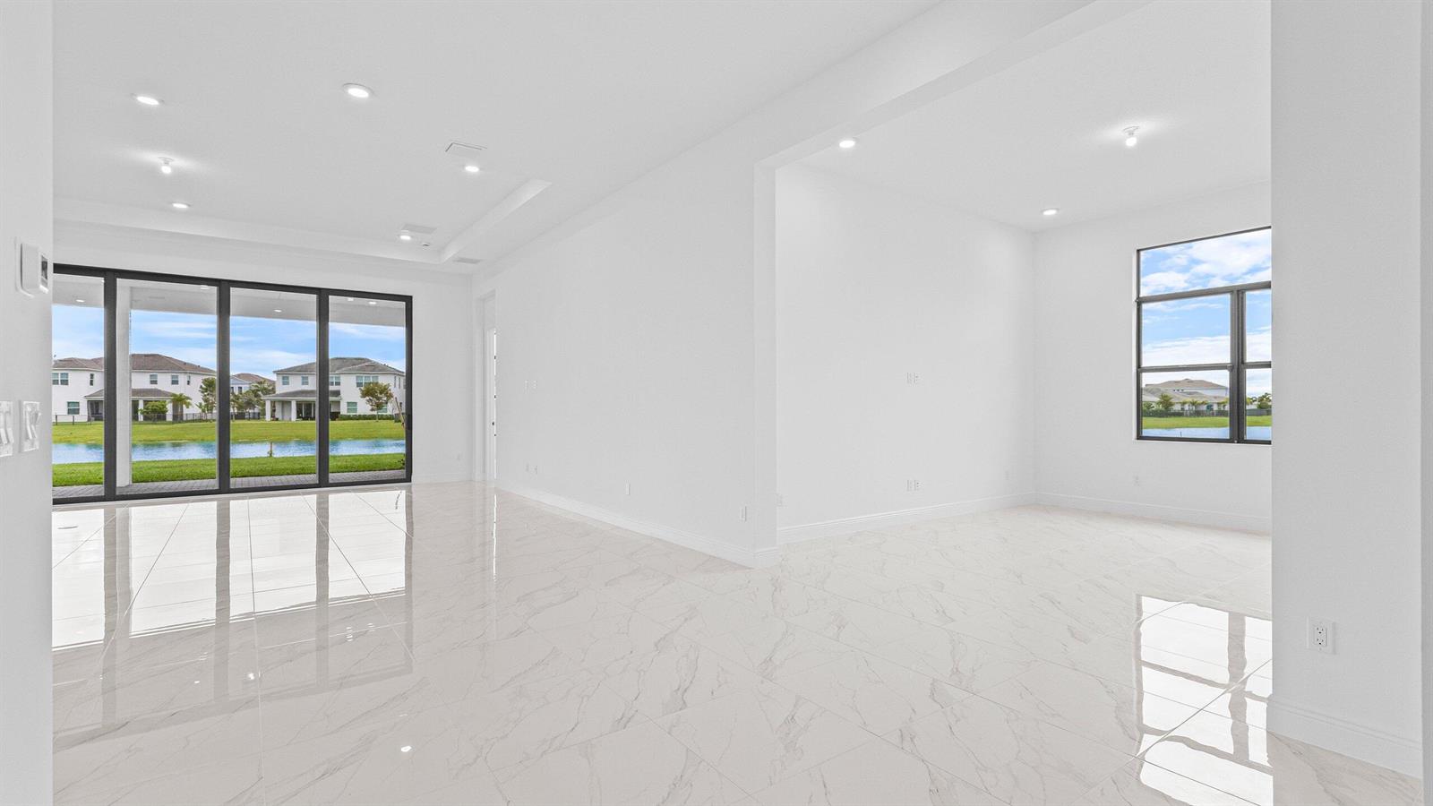 An empty room with white marble floors, recessed lighting, and large windows overlooking a lake — 5474 Hutchinson Way, FL 33470, FL