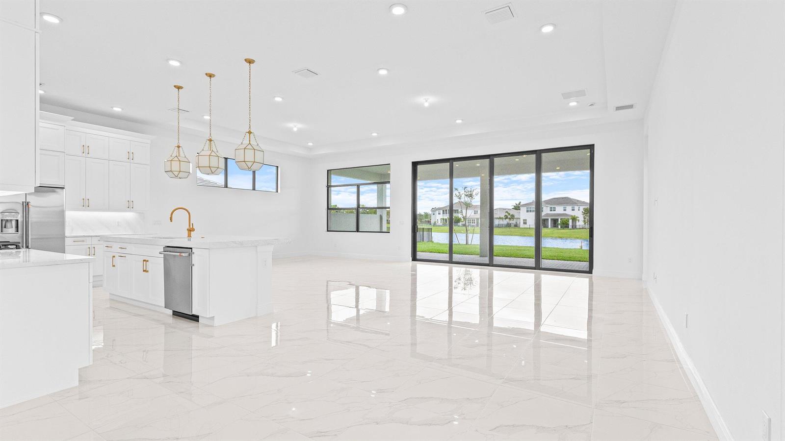 A bright, open-concept kitchen and living area features white cabinetry, marble-look tile, and sliding doors — 5474 Hutchinson Way, FL 33470, FL