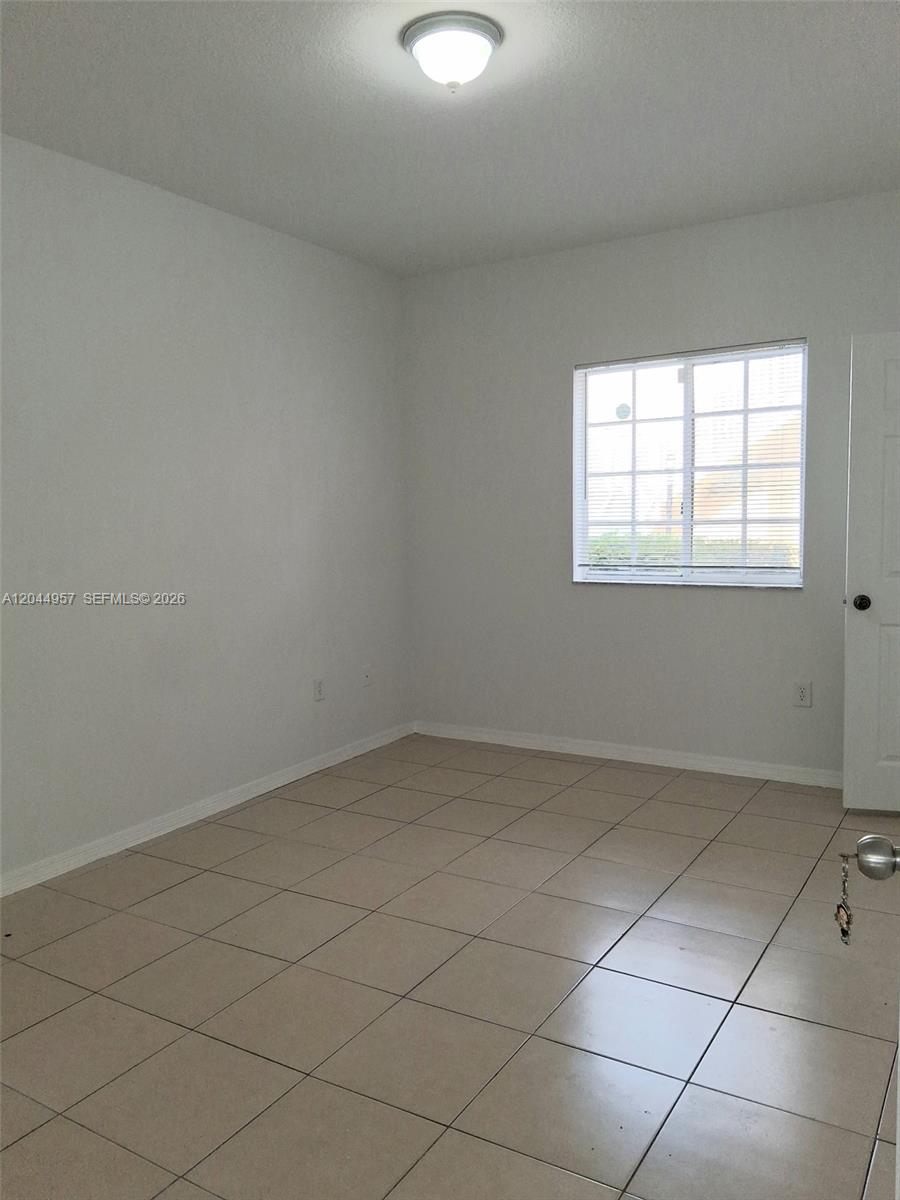 An empty room features light-colored tile flooring, white walls, a window, and a ceiling light — 6972 NW 179th St # 4, Hialeah FL 33015, HIALEAH, FL
