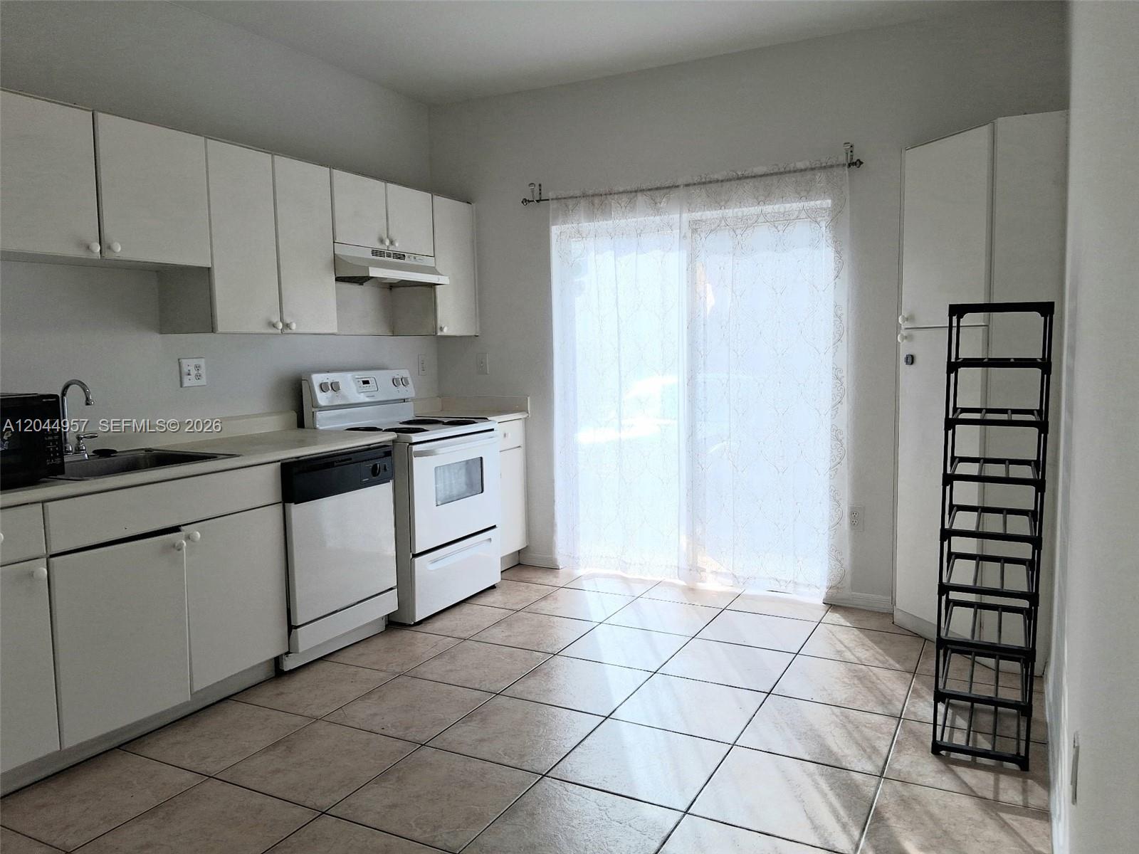 A kitchen features white cabinets, white appliances, tile flooring, and a sliding glass door — 6972 NW 179th St # 4, Hialeah FL 33015, HIALEAH, FL