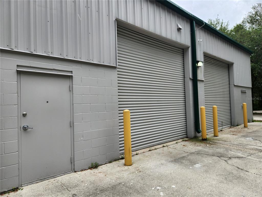 The exterior of a gray industrial building features a pedestrian door and two roll-up doors — 1607 S STATE ROAD 15A UNIT 11, DELAND, FL