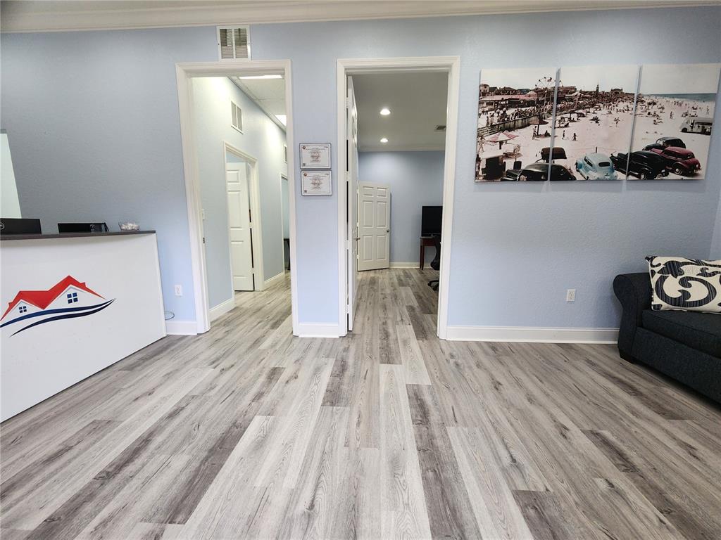 An office reception area features light blue walls, wood-look flooring, and two open doorways — 1607 S STATE ROAD 15A UNIT 11, DELAND, FL