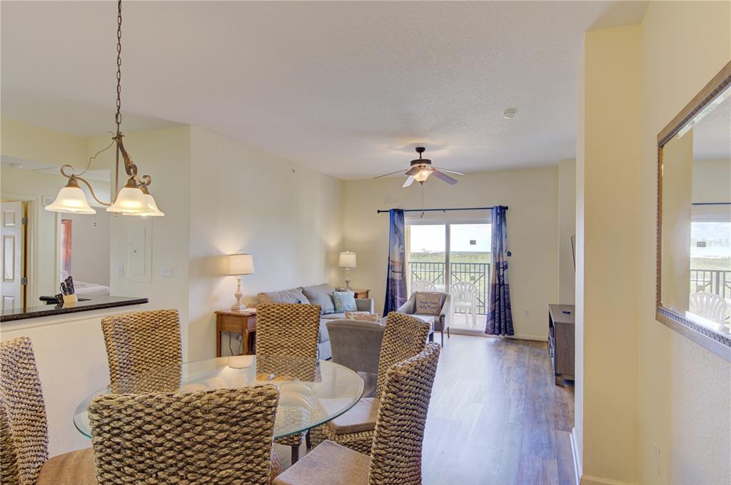 A dining area with a glass table and woven chairs opens into a living room — 8101 RESORT VILLAGE DRIVE UNIT 31101, ORLANDO, FL