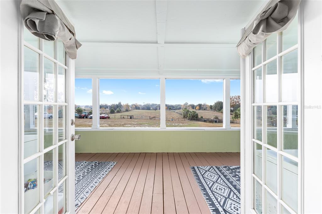 A covered porch with wooden flooring and large windows overlooks an open field — 13590 SE 120TH STREET, DUNNELLON, FL