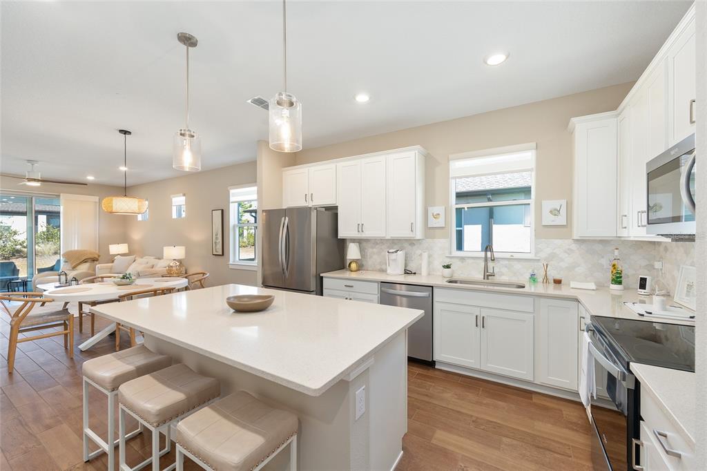 A kitchen with white cabinets, a quartz island, and stainless steel appliances opens to a dining area — 8919 SW 58TH STREET ROAD, OCALA, FL