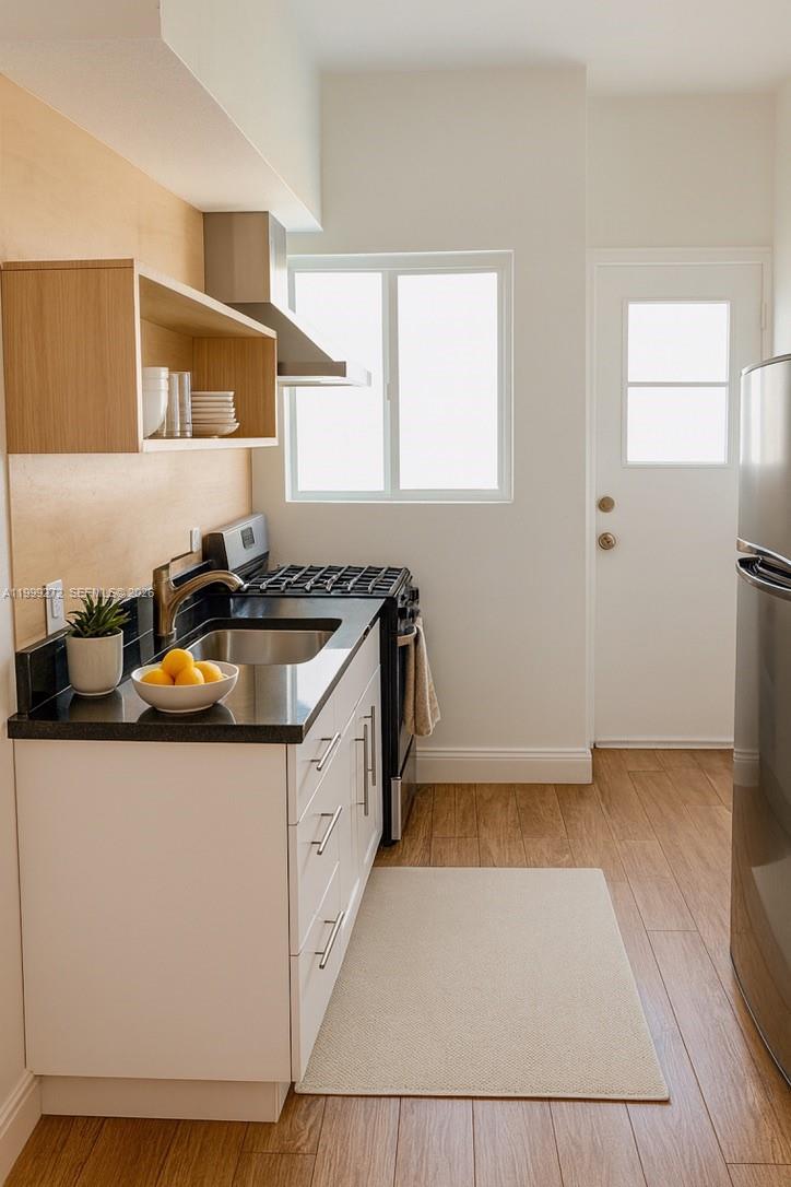 A modern kitchen features white cabinets, black countertops, a stainless steel stove, and wood flooring — 505 74th St # 6B, Miami Beach FL 33141, MIAMI BEACH, FL