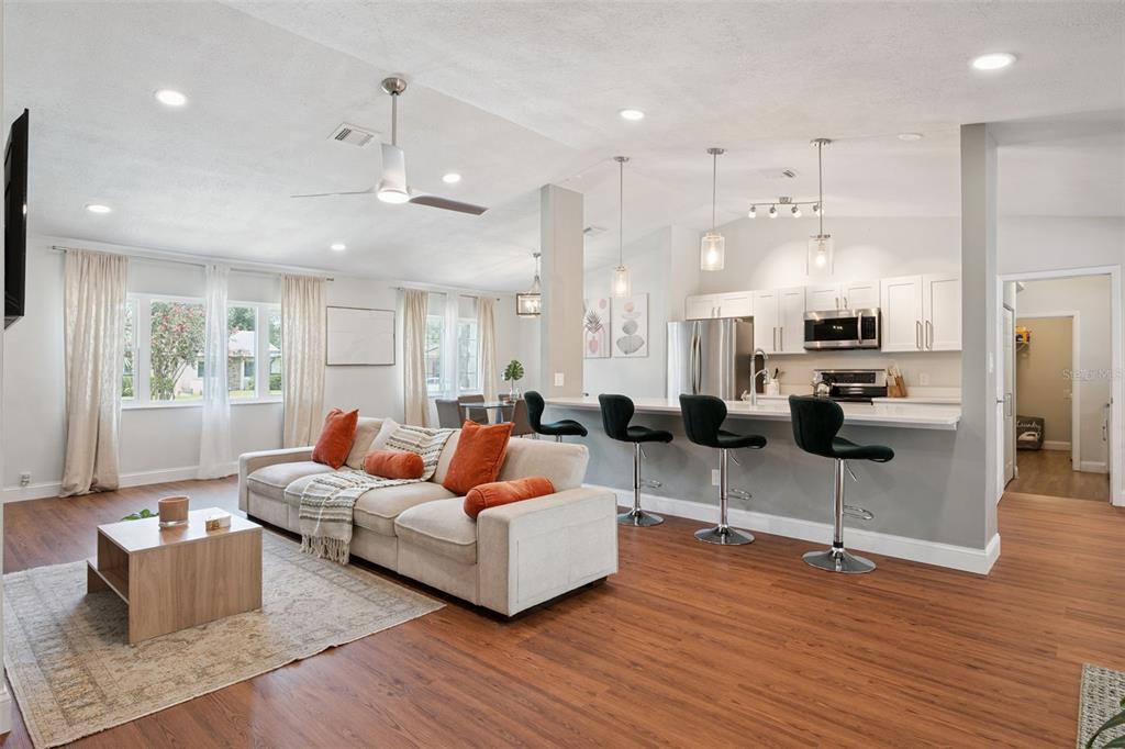 An open-concept living room and kitchen featuring a beige sofa, breakfast bar, and wood flooring — 8714 HILL PINE ROAD, ORLANDO, FL