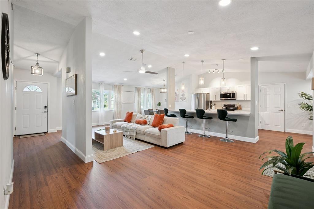 An open-concept living room and kitchen feature wood-look flooring, white cabinets, and a breakfast bar — 8714 HILL PINE ROAD, ORLANDO, FL