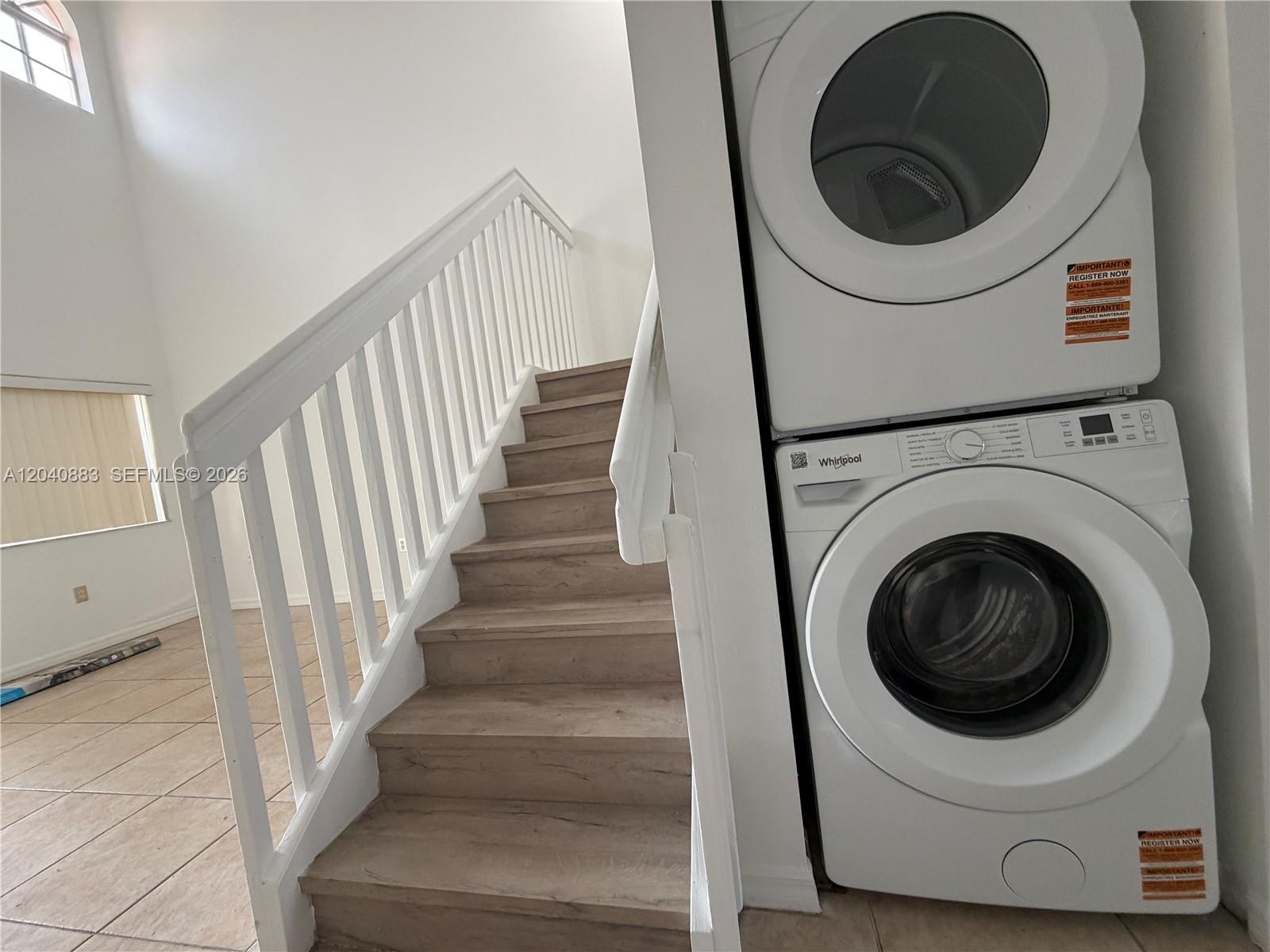 A white stacked washer and dryer unit sits beside a wooden staircase with white railings — 7245 NW 173rd Dr # 2505, Hialeah FL 33015, HIALEAH, FL