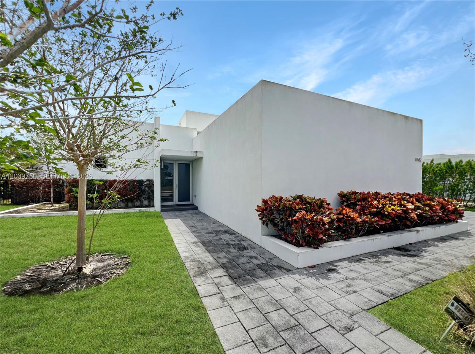 A modern white house features a paved walkway, a manicured lawn, and a landscaped garden bed — 16582 S Botaniko Dr S # 16582, Weston FL 33326, WESTON, FL