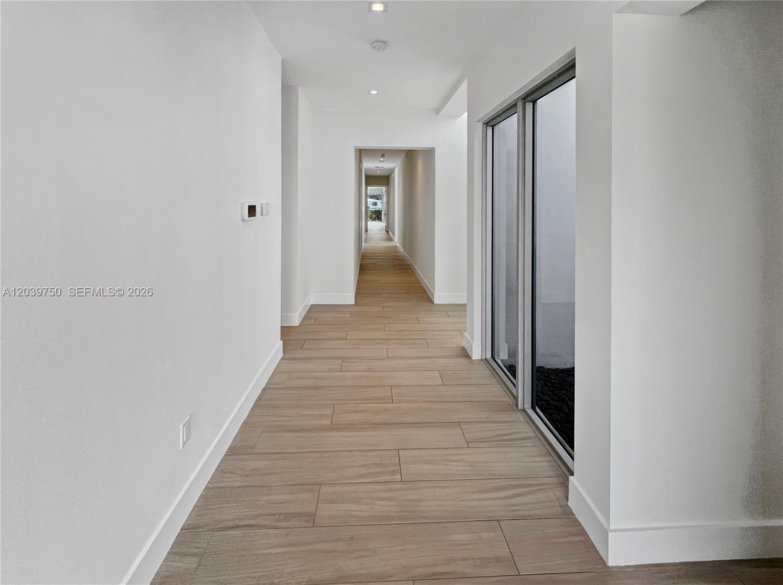 A long, minimalist hallway features light wood-look tile flooring and a glass-walled interior courtyard — 16582 S Botaniko Dr S # 16582, Weston FL 33326, WESTON, FL
